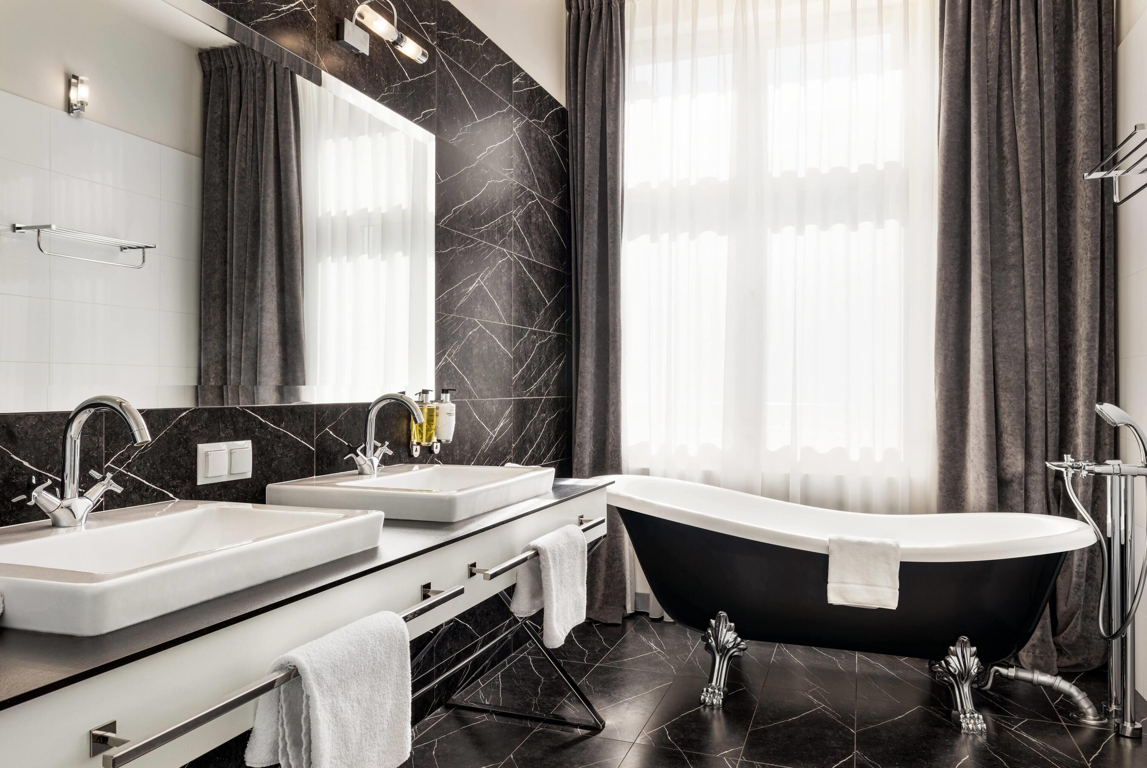 A modern bathroom with a freestanding bathtub, two sinks, a large mirror, and dark marble walls.