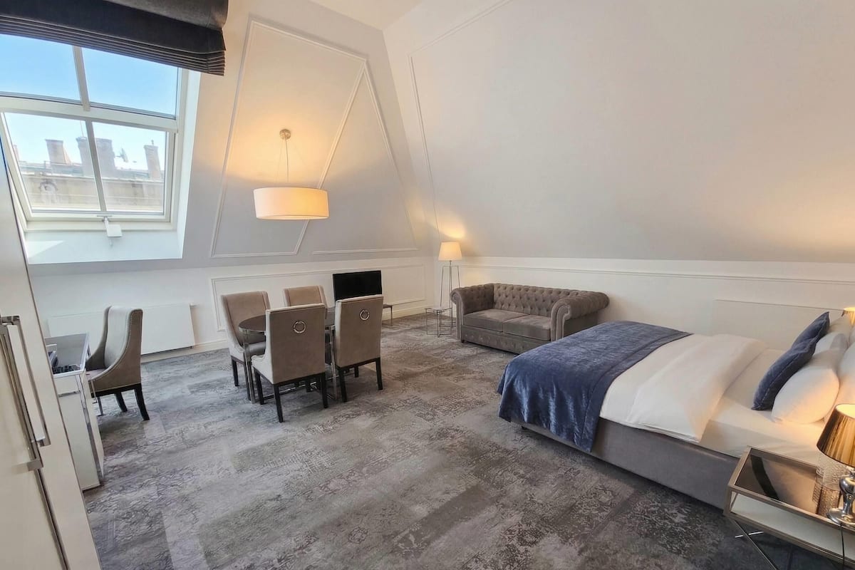 Hotellihuone, jossa on sänky, sohva, ruokapöytä tuoleineen, lamppu ja ikkuna.