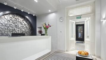 A reception area with a modern design, featuring a reception desk, a clock, and a sign indicating the direction to the elevator.
