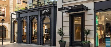 A building with a modern facade, featuring a black awning and a sign for 'Trattoria Degust'.