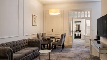 A living room with a sofa, chairs, a small table, a TV, and a door leading to a bathroom.