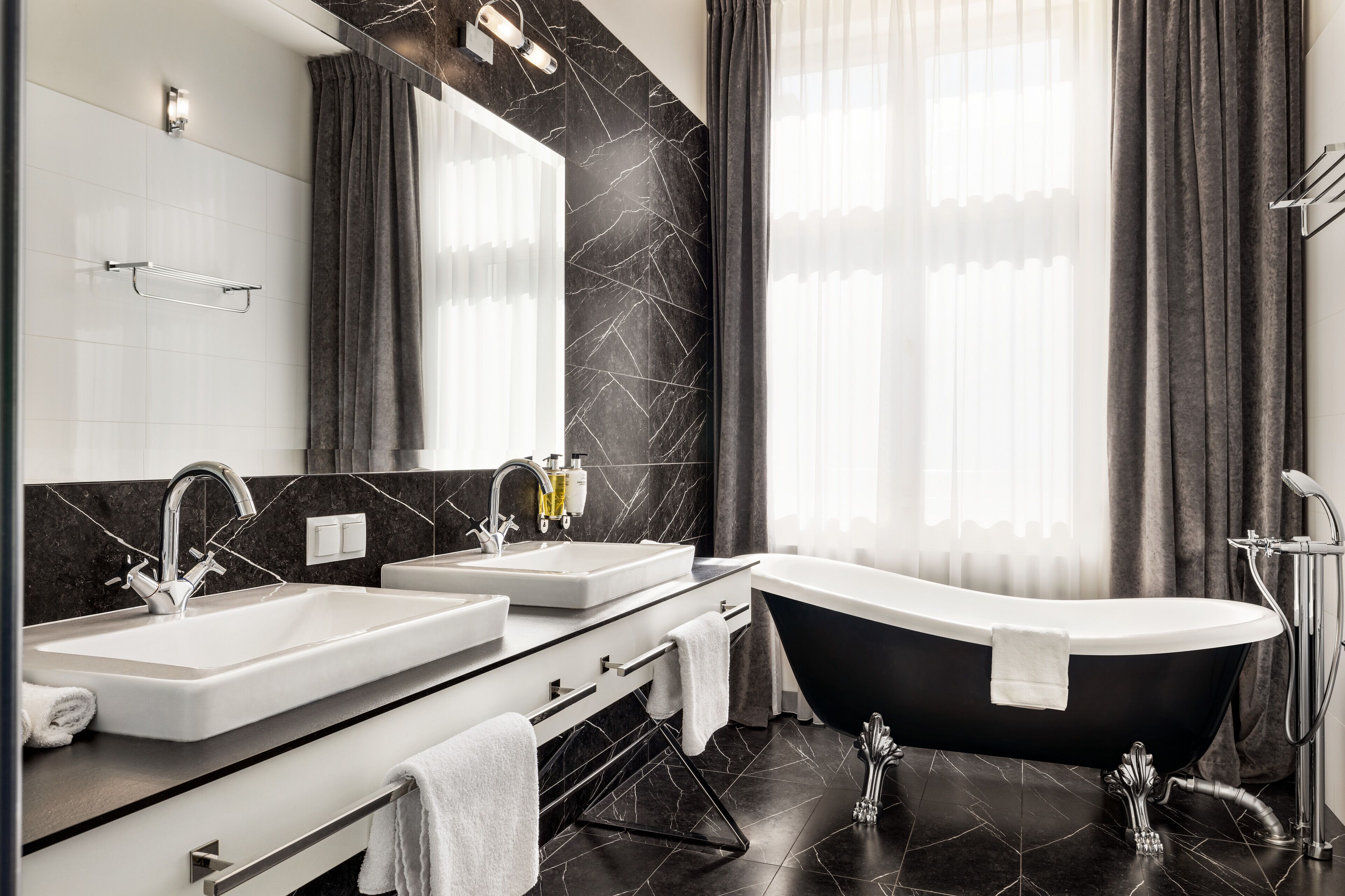 A modern bathroom with a black bathtub, two sinks, a large mirror, and a shower area.
