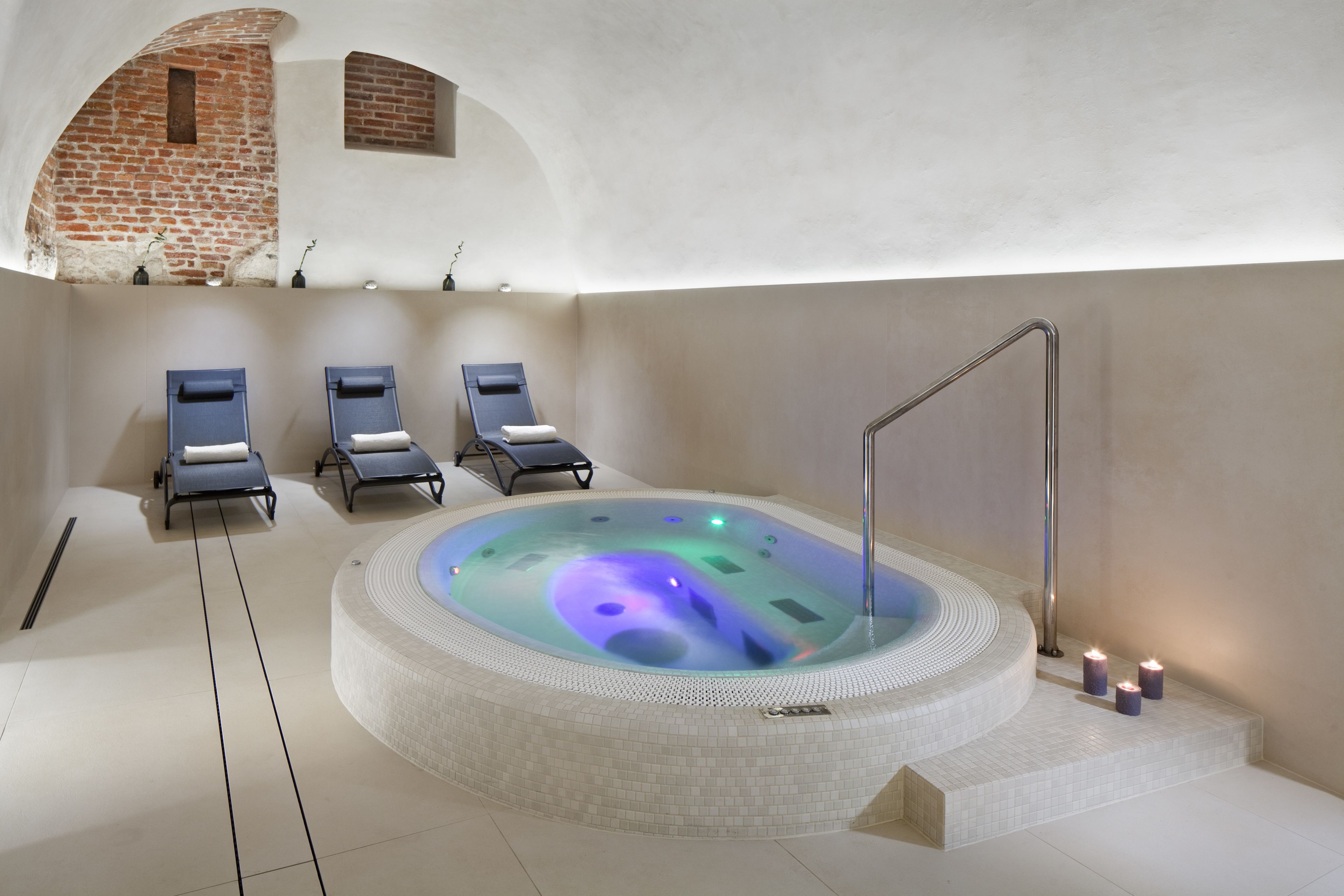 A spa area with a hot tub, lounge chairs, and a brick wall.