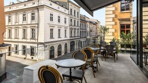 Un balcon doté de fauteuils et d’une table en osier, offrant une vue sur une rue bordée de bâtiments historiques.