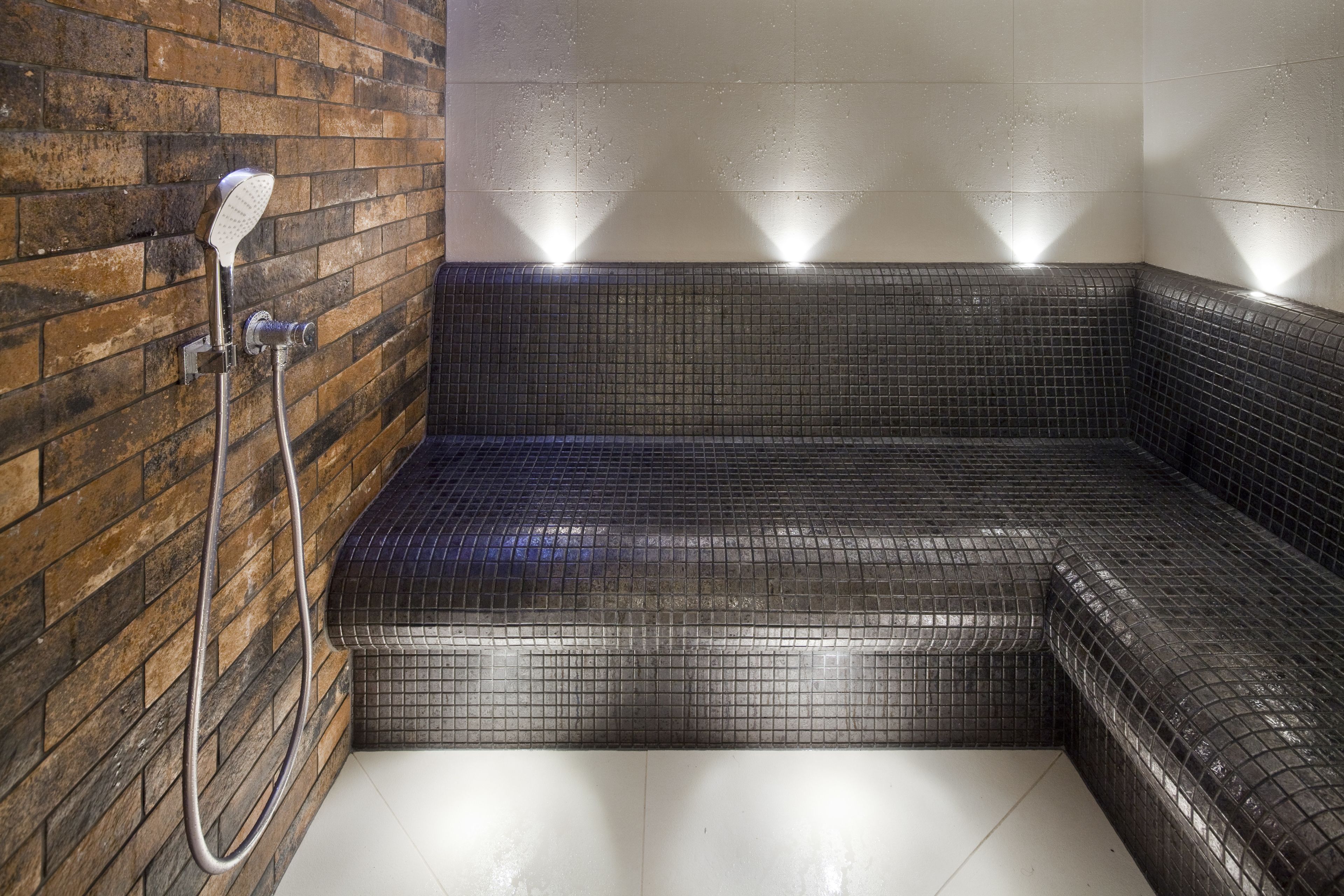 Ducha en esquina con pared y piso cubiertos de azulejos, un cabezal de ducha y una perilla de control.