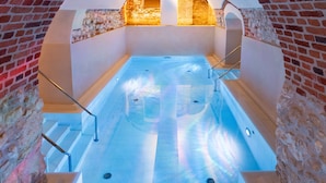 A hot tub with a stone wall and arched ceiling, surrounded by a brick wall.