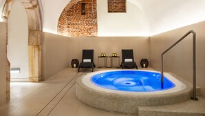 A spa area with a hot tub, two lounge chairs, and a brick wall.