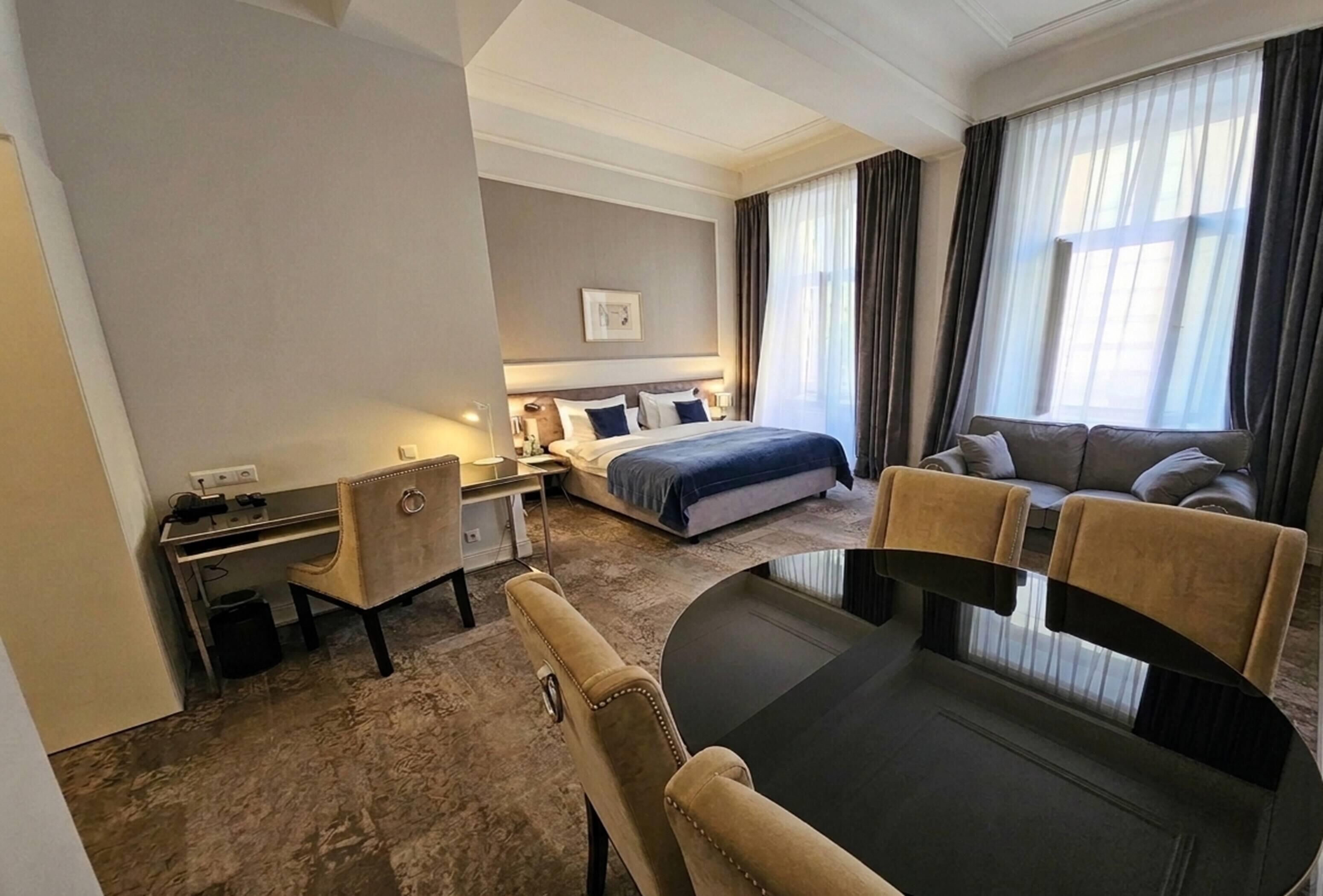 A hotel room with a bed, a desk, a sofa, and a dining table.