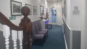 A hallway with a staircase, framed pictures on the walls, a fire exit sign, and a blue-lit reception desk. - The Mornington Hotel (Blackpool)