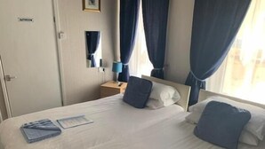 A hotel room with a bed, a nightstand, a lamp, and a bathroom sign. - The Mornington Hotel (Blackpool)