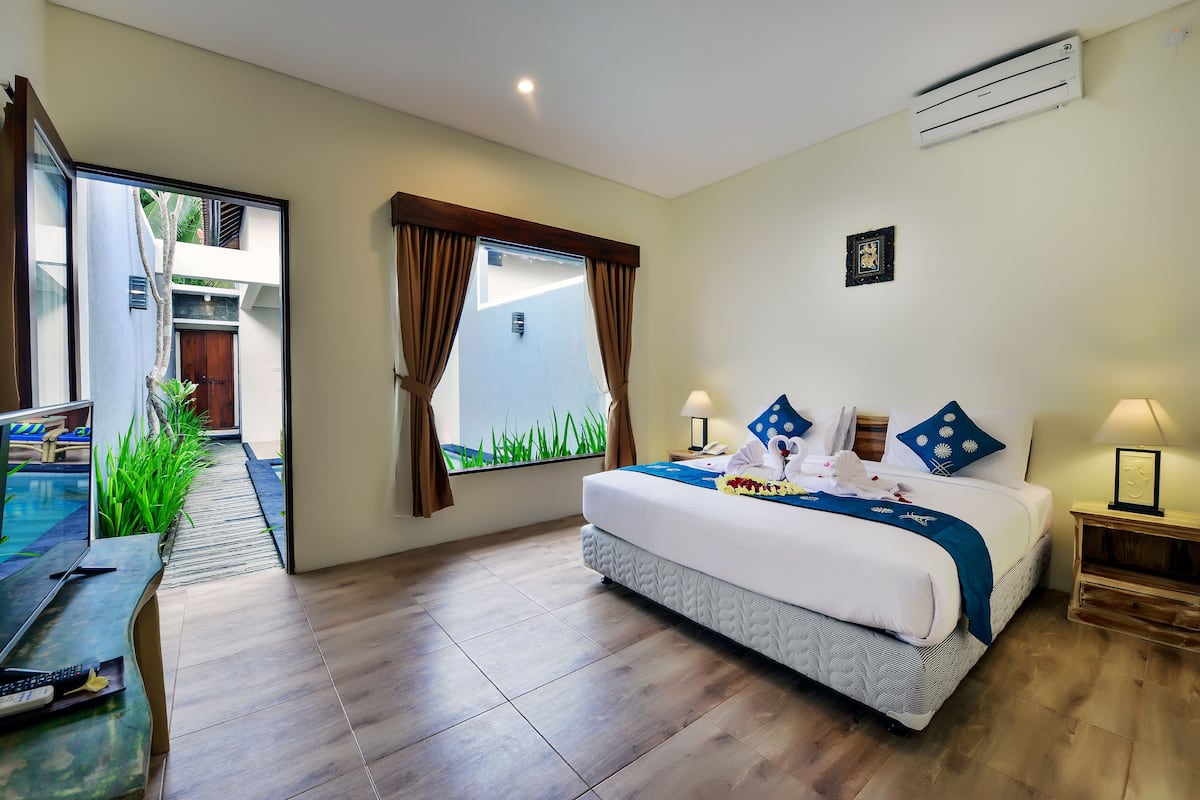 Habitación de hotel con cama, mesitas de noche, escritorio y vistas a una piscina y zona exterior.