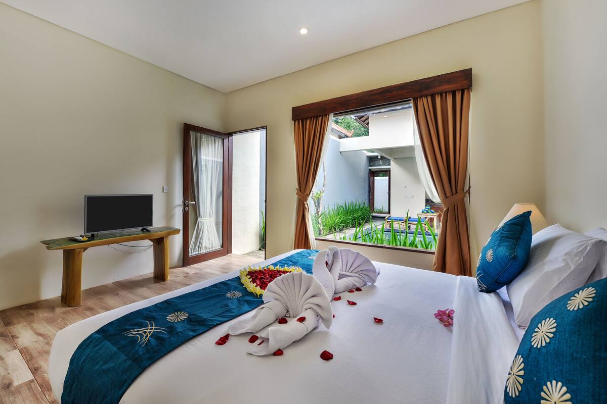 Habitación de hotel con cama, televisor sobre un soporte de madera y ventana con cortinas.