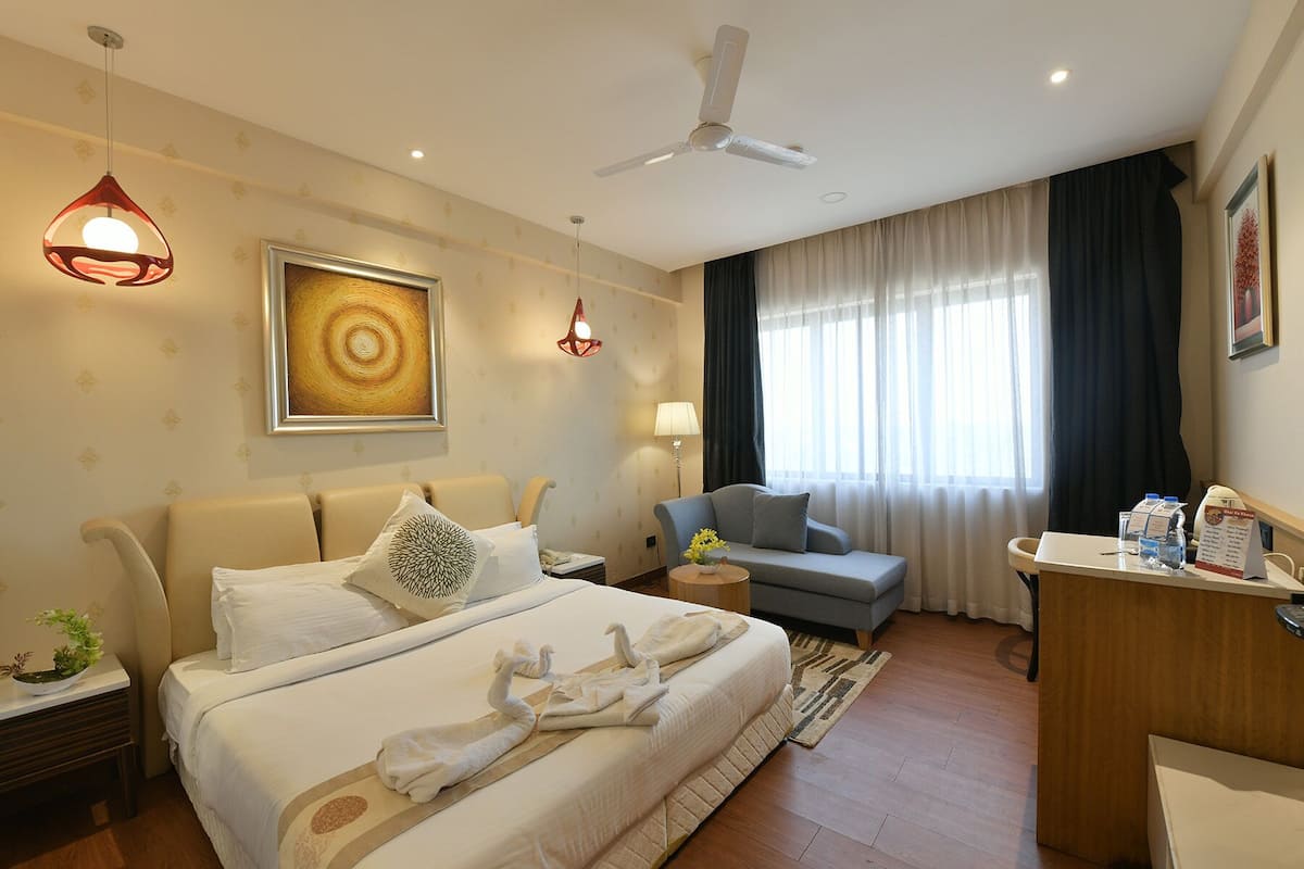 A hotel room with a bed, a sofa, a desk, a ceiling fan, and a window with curtains.