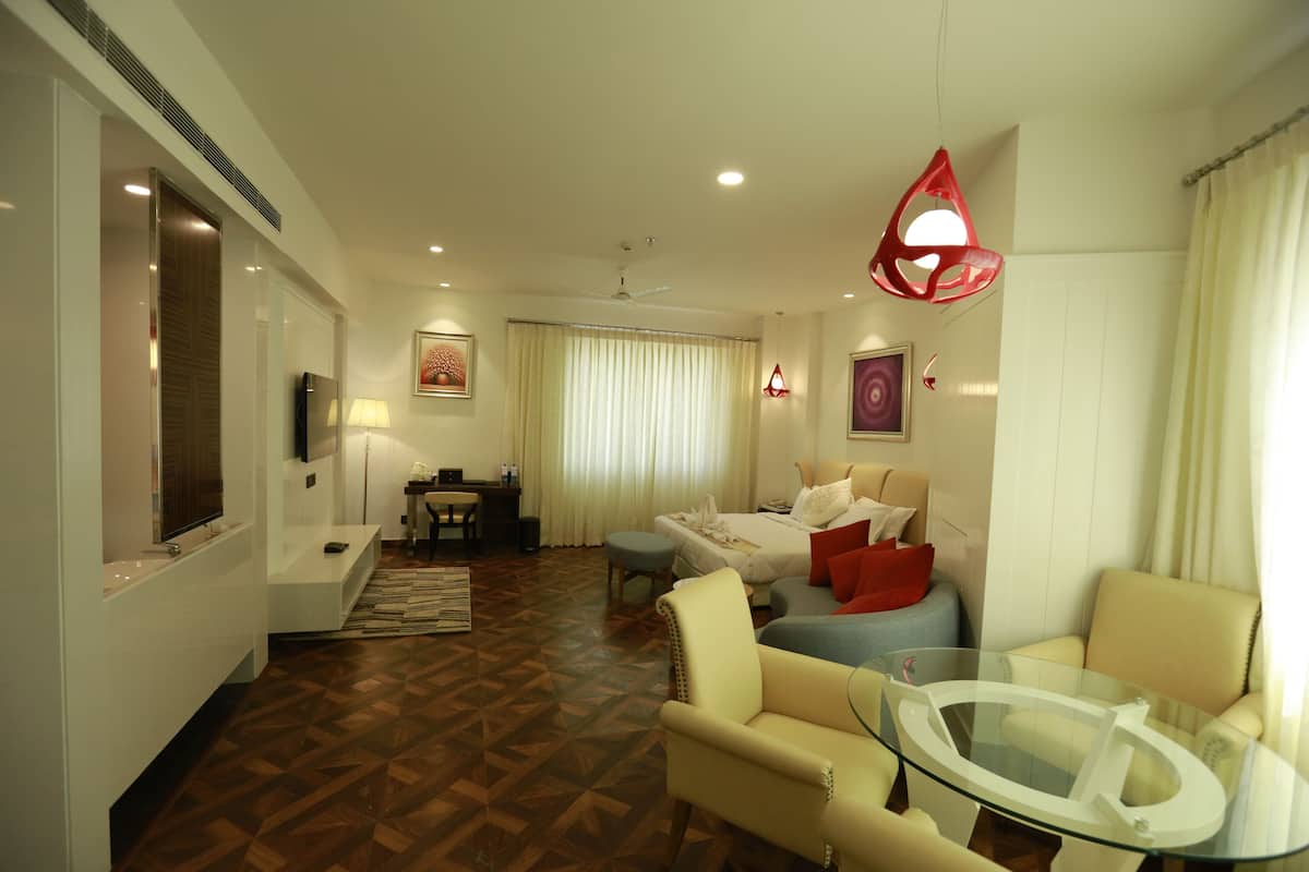 A modern hotel room with a wooden parquet floor, a glass coffee table, a sofa, a bed with red pillows, a TV, and a ceiling fan.