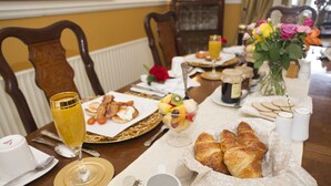 Une table en bois dressée pour le petit-déjeuner, avec des croissants, des fruits et un verre de jus d’orange.