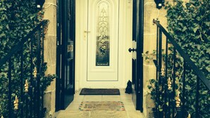 Une porte d’entrée avec une porte blanche, un panneau de verre décoratif et une rambarde en métal noir sur le côté gauche.