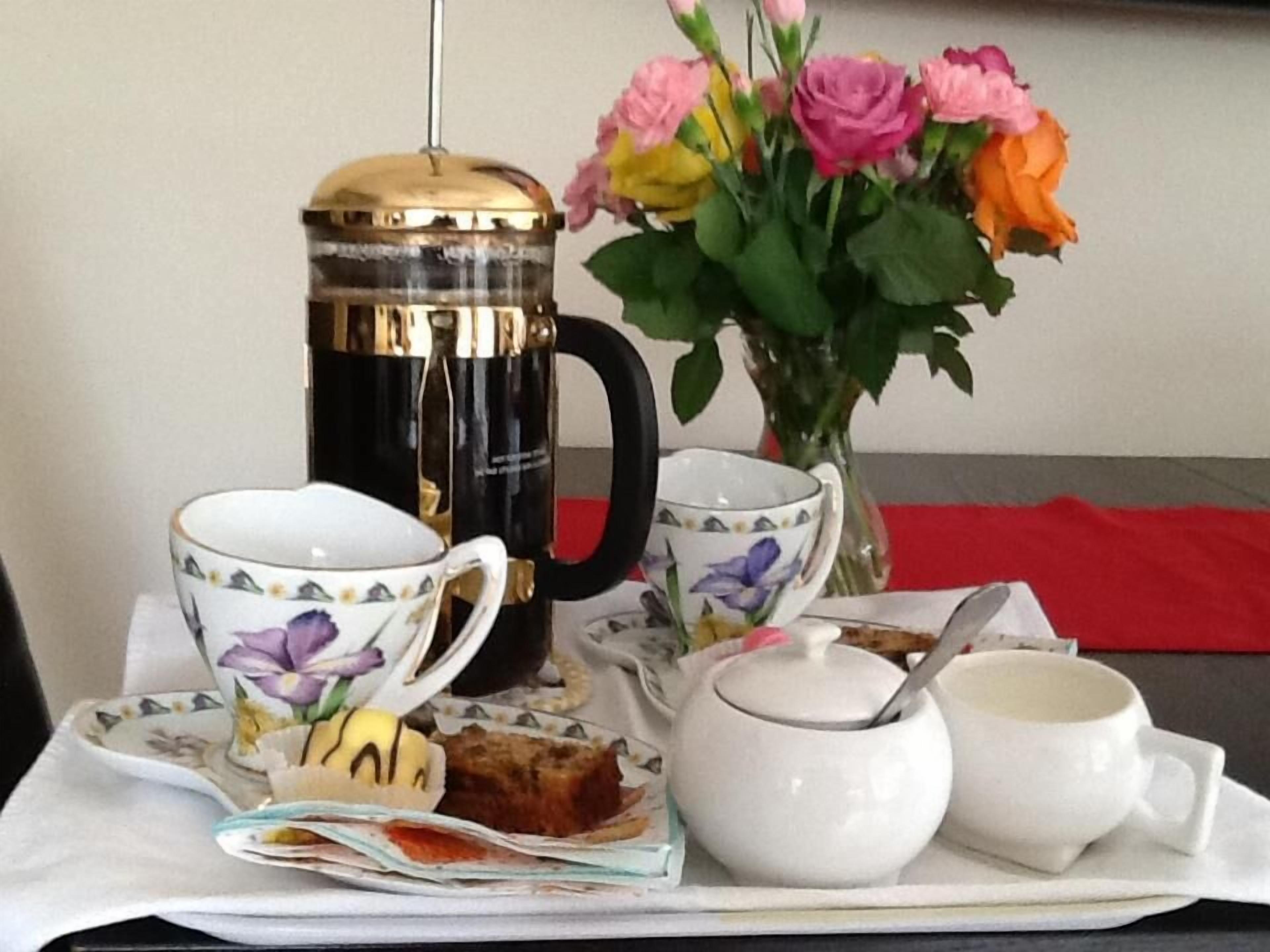A table with a coffee maker, teapot, cups, a vase with flowers, and a plate with a pastry.