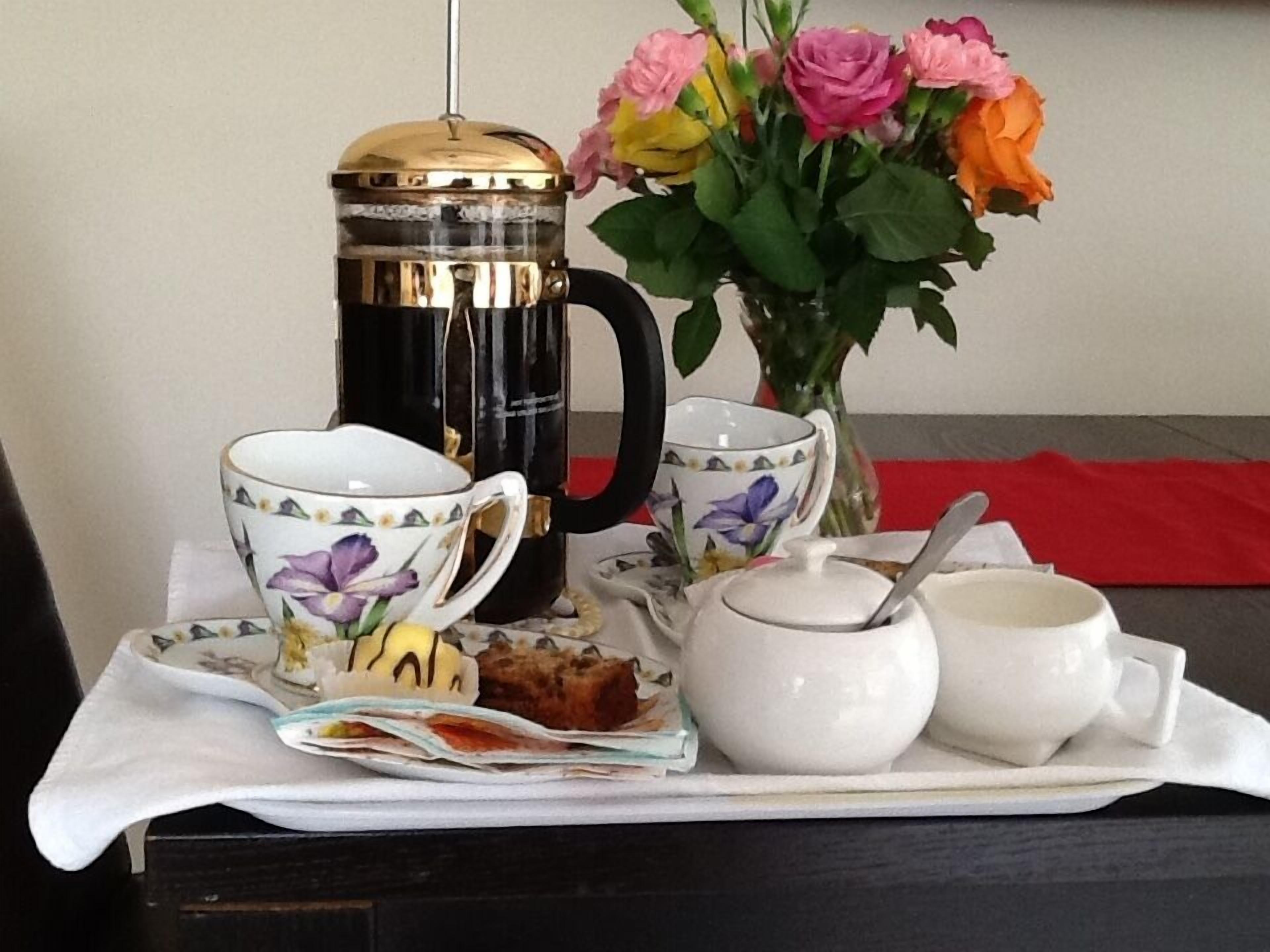 A tray with a coffee maker, teacups, a sugar bowl, a spoon, and a floral vase with roses.