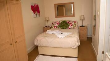 A bedroom with a bed, a nightstand, a dresser, a mirror, and a floral artwork on the wall.
