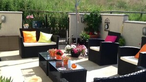 Une terrasse extérieure avec des meubles en osier, un parasol jaune et des plantes en pot.