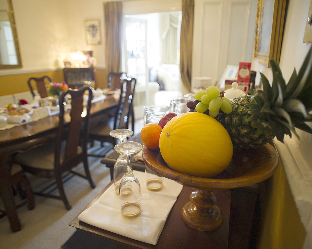 Una mesa de comedor con un frutero que contiene una piña, uvas, una naranja y un limón.