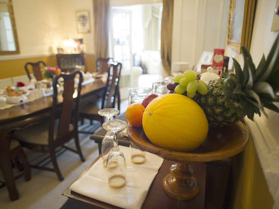 Una mesa de comedor con un frutero que contiene una piña, uvas, una naranja y un limón.