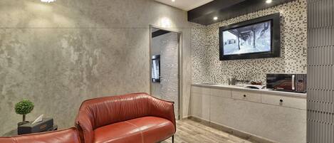A modern kitchen with a built-in microwave, a large flat-screen TV mounted on the wall, and a seating area with a leather sofa.