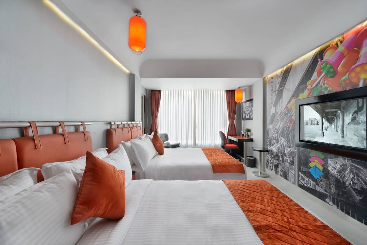 Ett hotellrum med två sängar, ett skrivbord, en stol och ett stort fönster med gardiner.