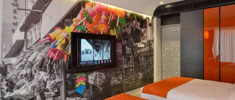 A hotel room with a bed, a television mounted on the wall, and a colorful wall decoration.