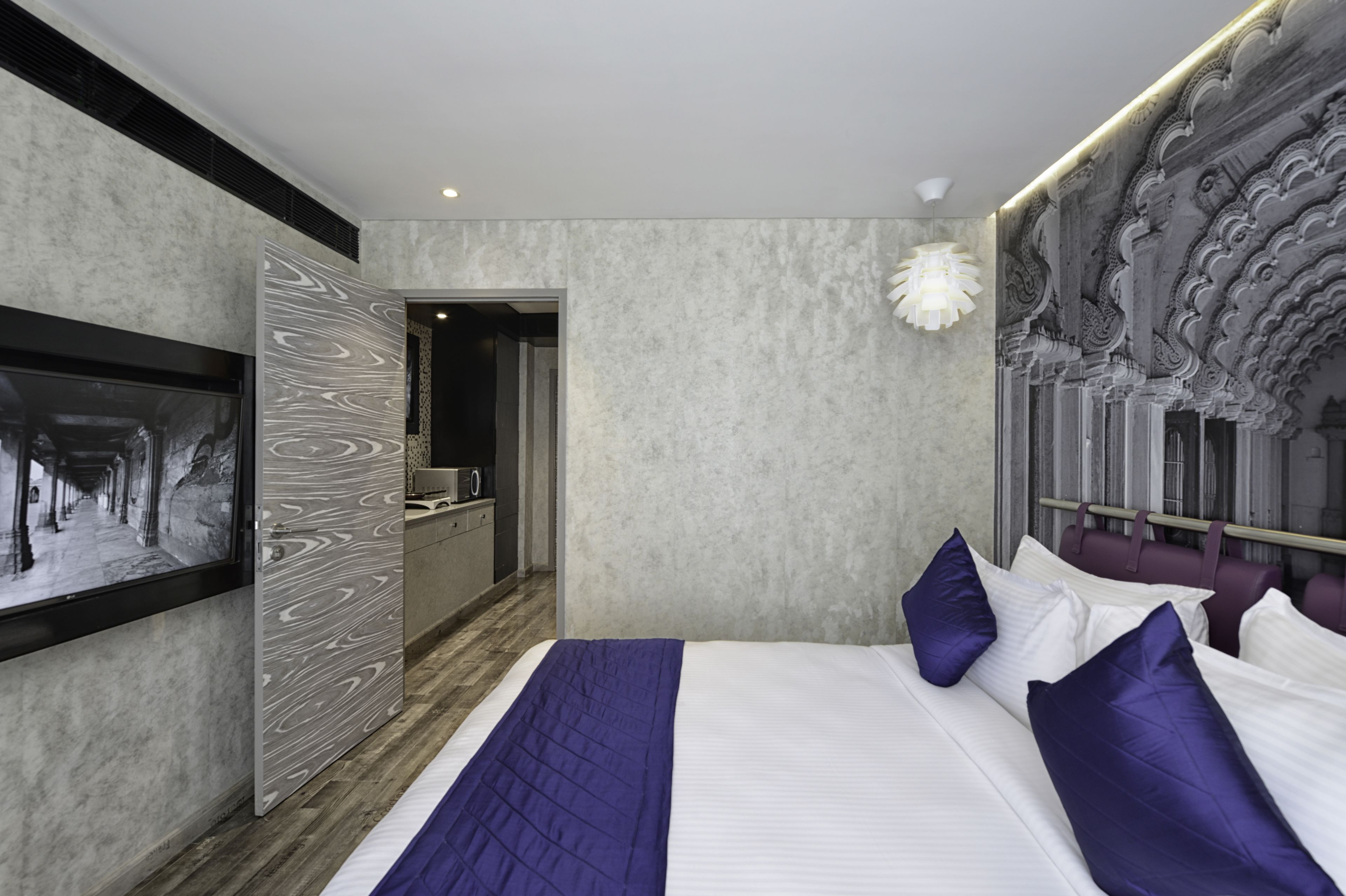 A modern hotel room with a large bed, a television on the wall, and a bathroom visible through an open door.