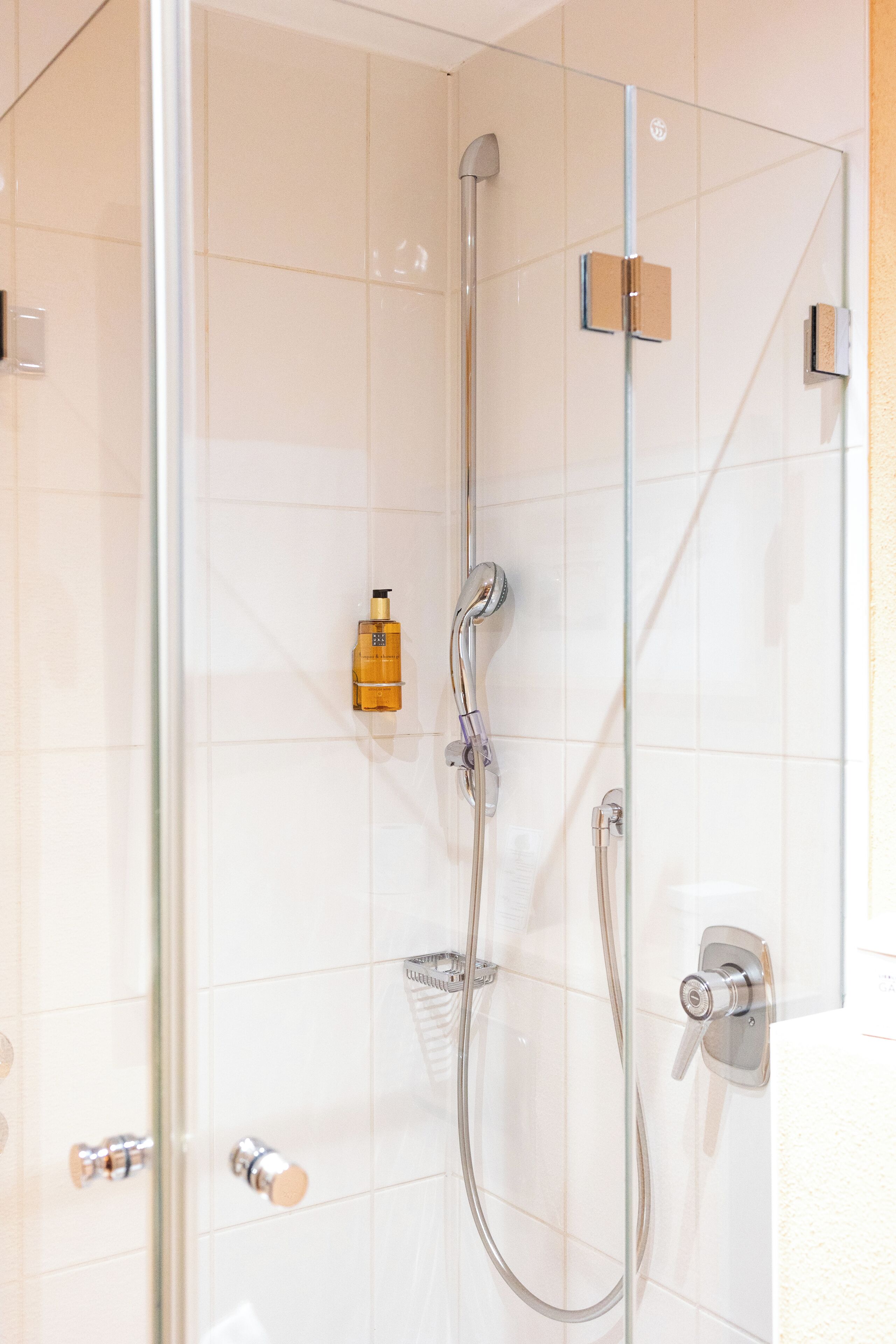 Ducha con cerramiento de vidrio, cabezal de ducha de mano y grifo empotrado.