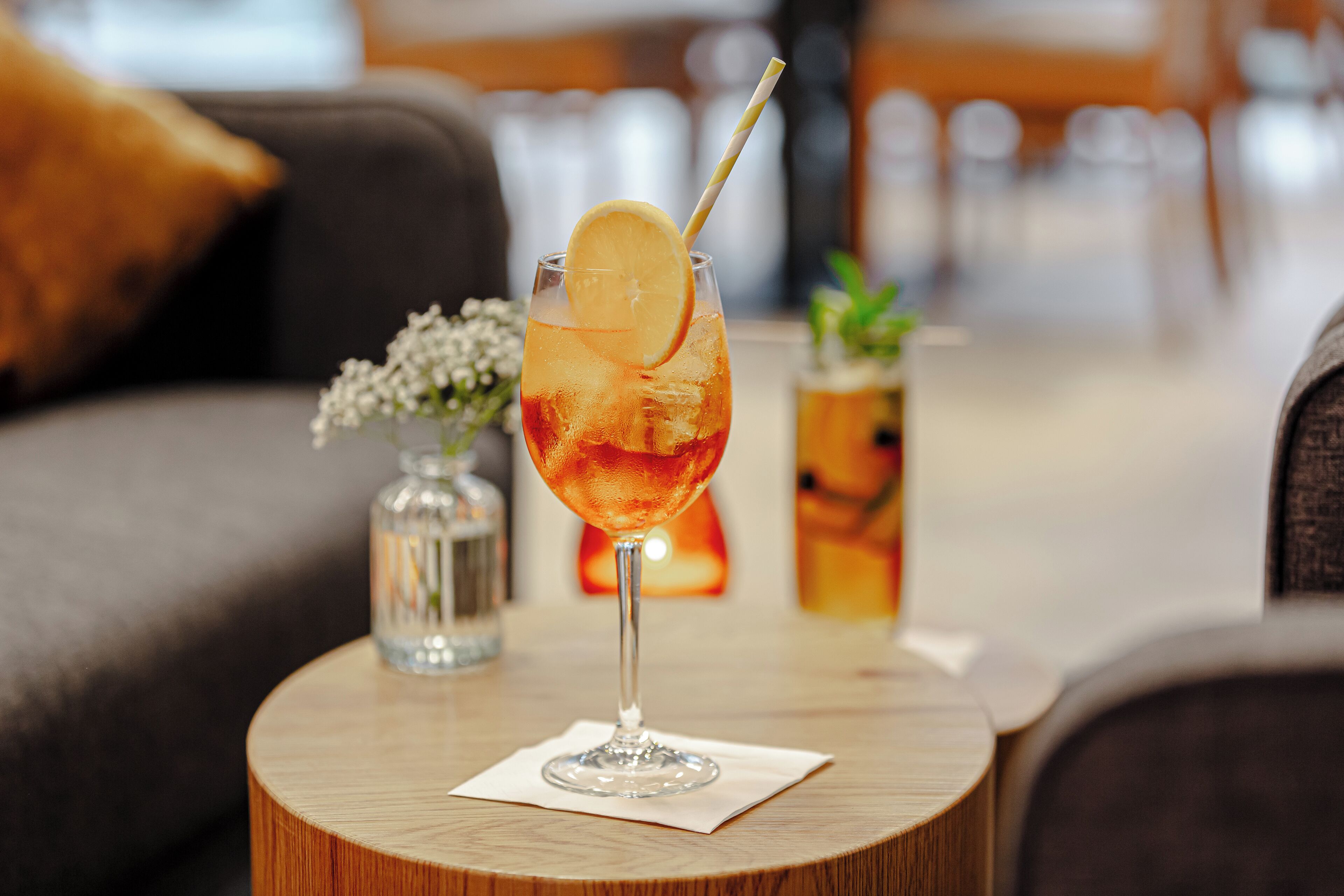 Un verre à cocktail, orné d’une tranche de citron et d’une paille, est posé sur une table en bois dans un cadre intérieur chaleureux et accueillant.