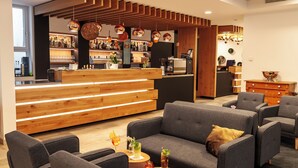 Un espace bar moderne avec un comptoir en bois, des sièges avec des canapés gris et un sol recouvert d’un tapis noir.