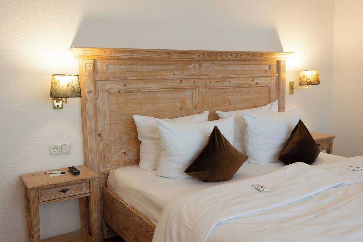 Un lit bien fait, avec du linge de lit blanc et deux oreillers marron, une tête de lit en bois et deux lampes de chevet.