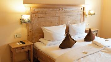 A neatly made bed with white linens, two pillows, and a remote control on a wooden nightstand.