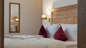Un lit bien fait, avec du linge de lit blanc et deux oreillers rouges, une tête de lit en bois, un miroir fixé au mur et une lampe de chevet.