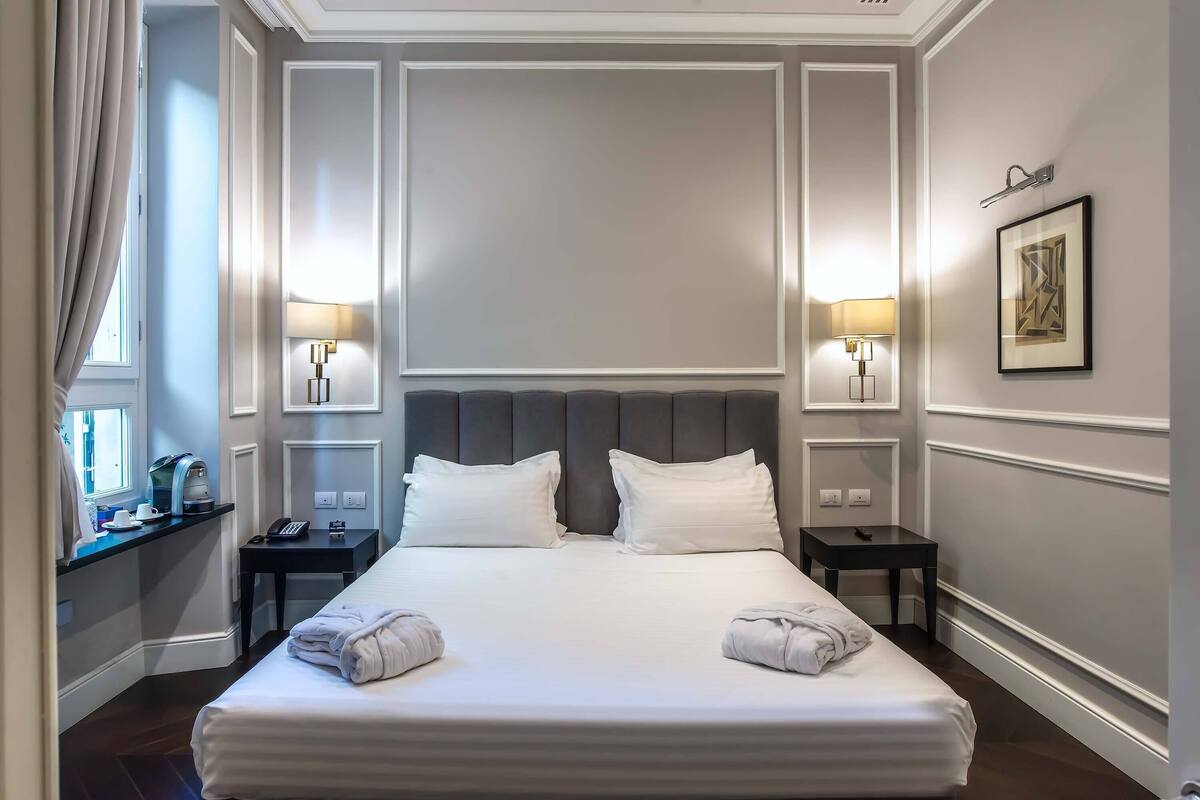 A hotel room with a large bed, two bedside tables, a nightstand, a window with curtains, and a framed picture on the wall.