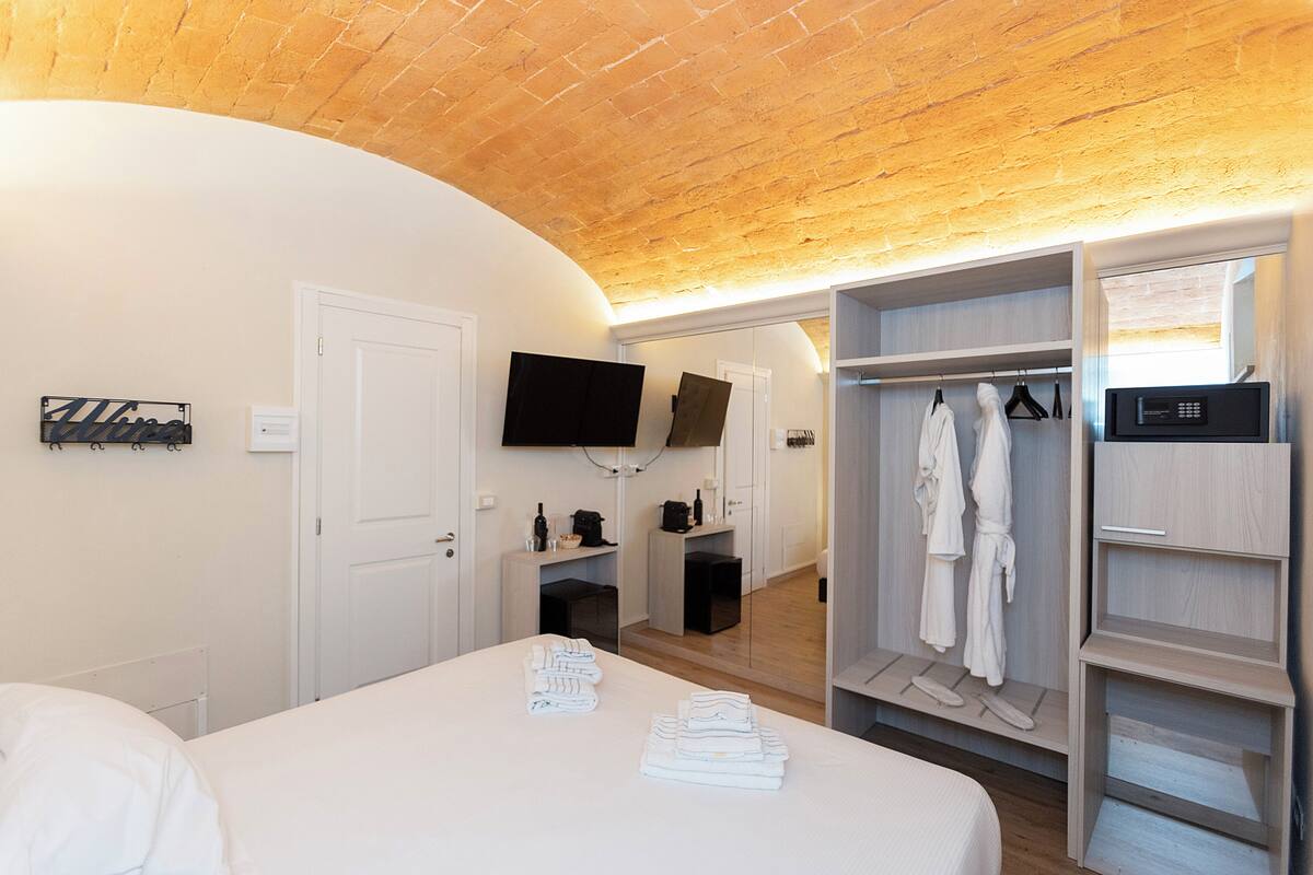 A hotel room with a bed, a TV mounted on the wall, a wardrobe, and a small seating area with a table and chairs.