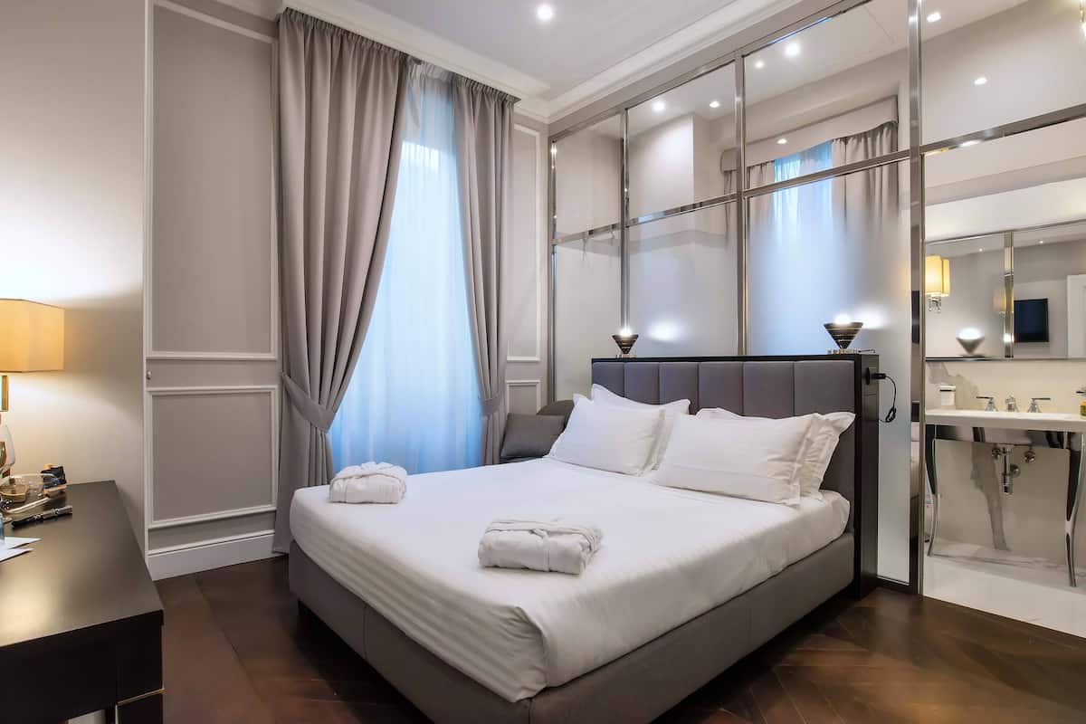 A modern hotel room with a large bed, a desk, and a bathroom with a glass shower enclosure.