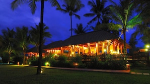 Un resort con un edificio de techo de paja, rodeado de palmeras y senderos bien iluminados.