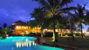 Un resort con piscina, palmeras y un edificio con ventanas iluminadas por la noche.