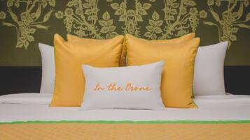 Una cama con almohadas blancas y amarillas, una colcha verde y un estampado floral en el papel tapiz.