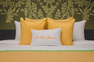 Una cama con almohadas blancas y amarillas, una colcha verde y un estampado floral en el papel tapiz.