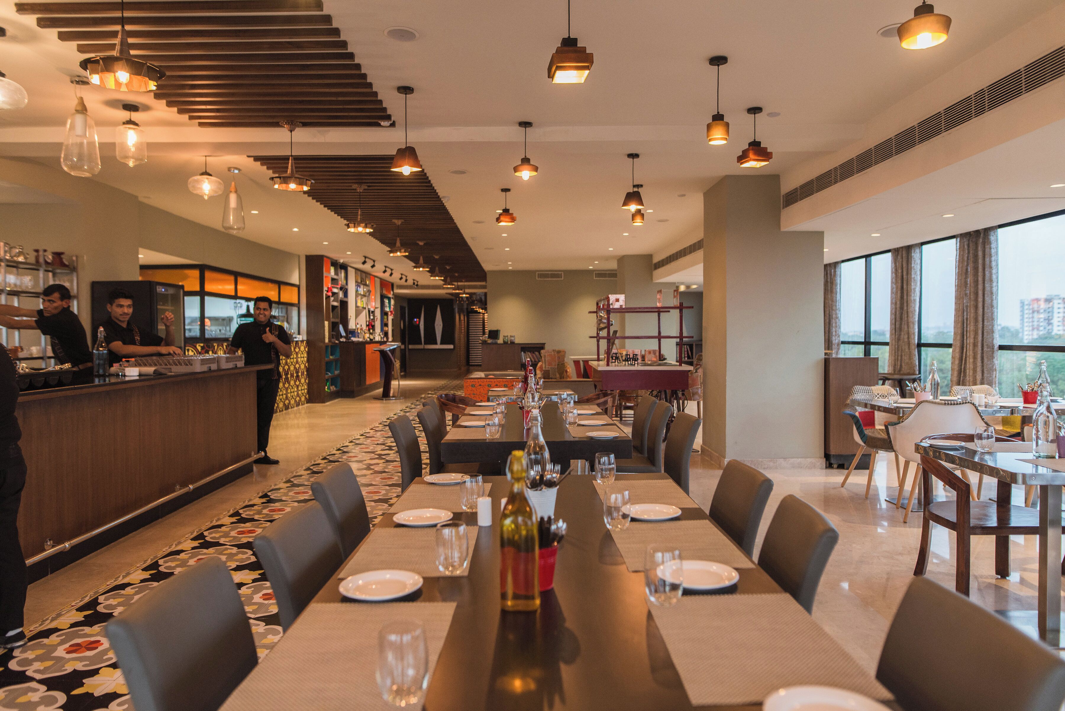 Un restaurante moderno con una larga mesa de comedor lista para una comida, una zona de bar y vistas de la ciudad a través de amplios ventanales.