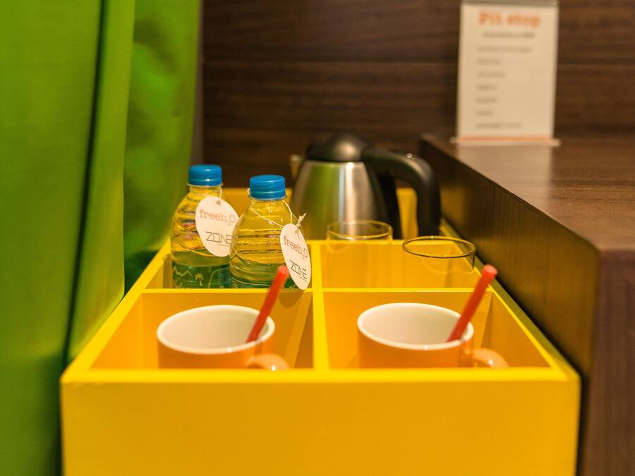 Zona de recepción de hotel con una bandeja amarilla que contiene dos botellas de agua, dos vasos con pajitas y una tetera.