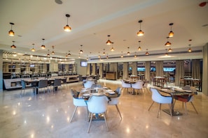 En moderne hotellobby med flere spiseområder, en reception og et tv-skærm.