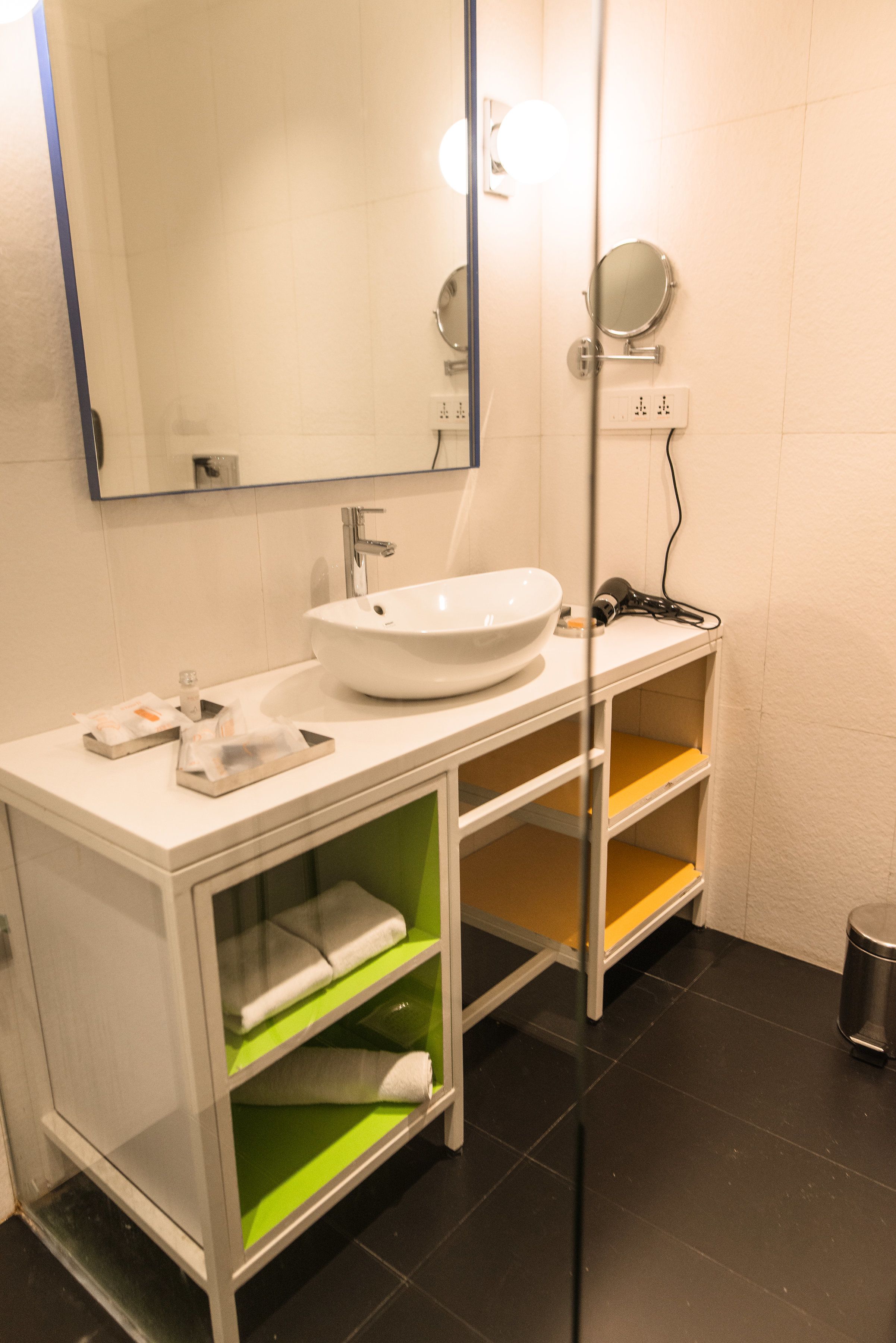 A modern bathroom with a white sink, mirror, and green shelves.