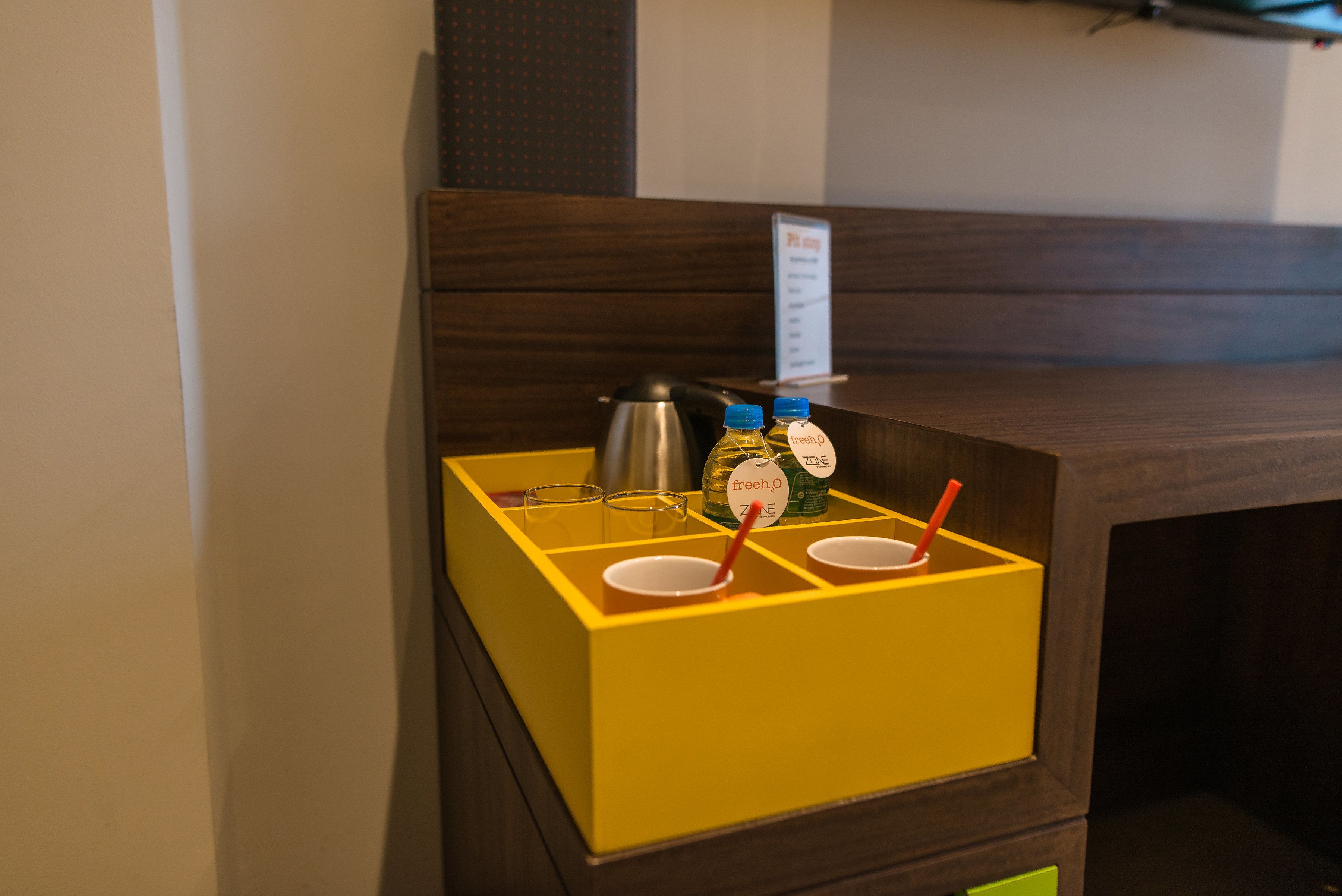 A yellow minibar with a coffee pot, two bottles of water, and two cups with straws.