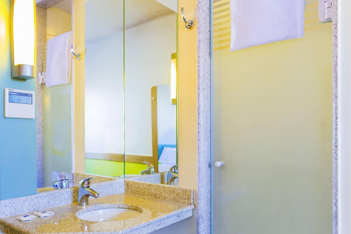 Un baño con lavamanos de encimera de granito, espejo y toalla colgada en la pared.