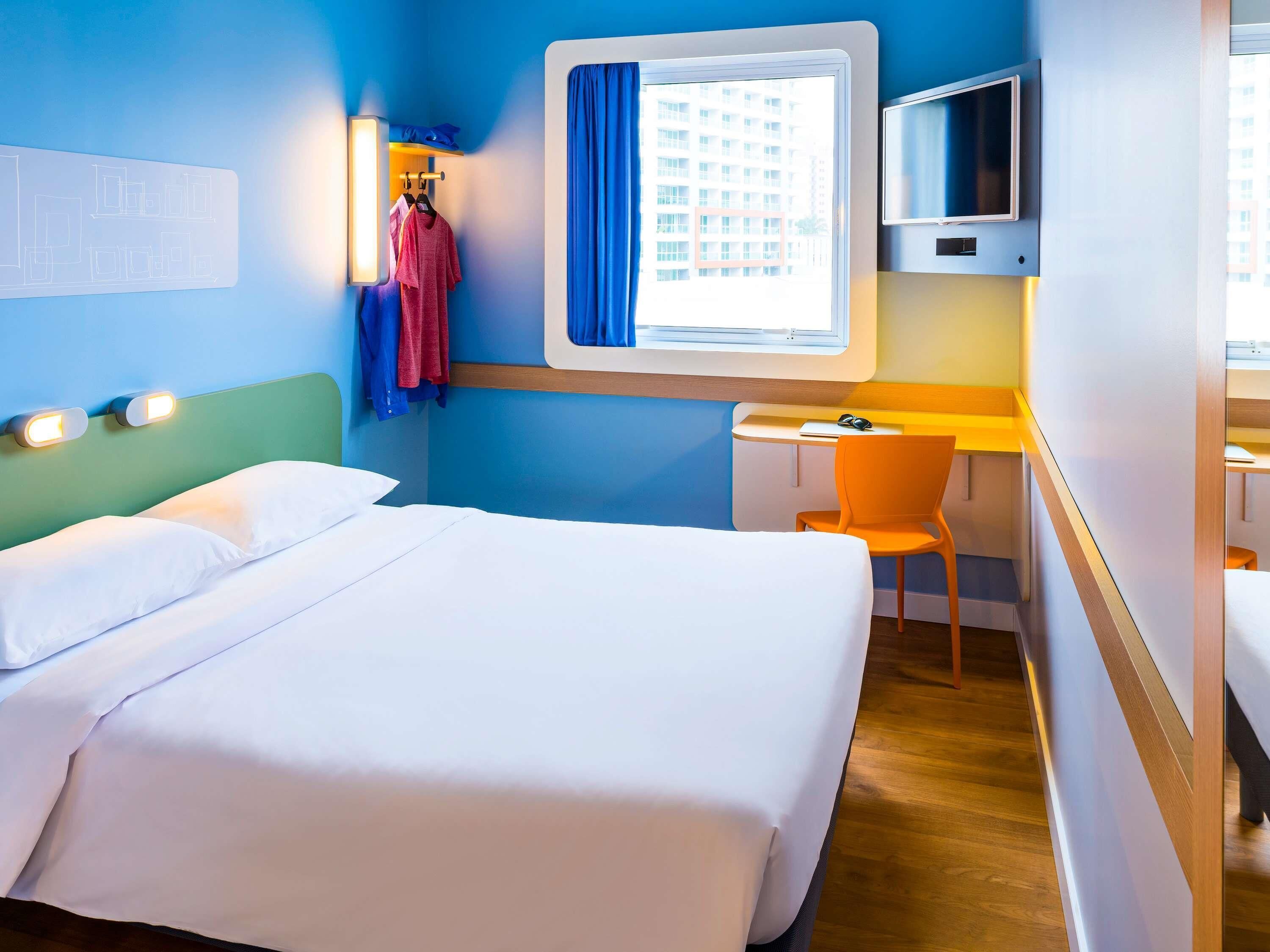 Een hotelkamer met een bed, een bureau, een stoel, een televisie en een raam met gordijnen.